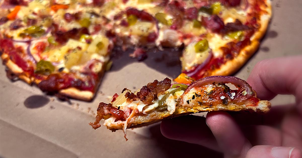 Closeup image of a slice of Lake Country Supreme thin-crust pizza held up to show the thinness of the crust and thickness of the toppings. 